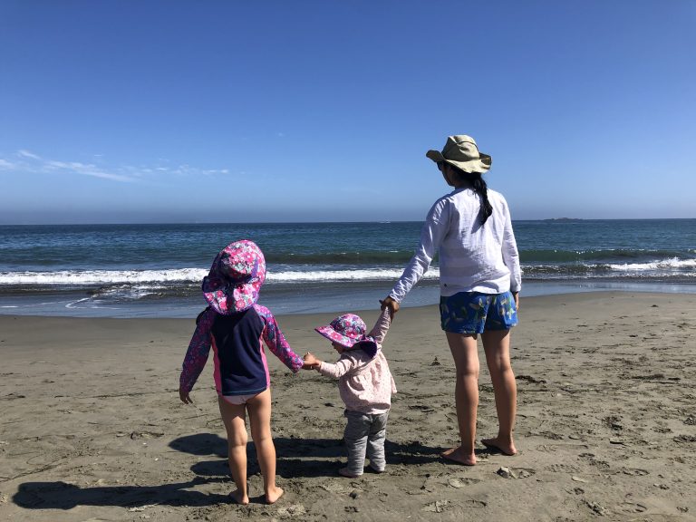 An adult holding hands with two little kids on the sand at Doran Beach near the campground in Bodega Bay