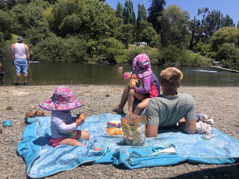 A family on a blanket on the riverbank of Russian River at Casini Ranch Family Campground