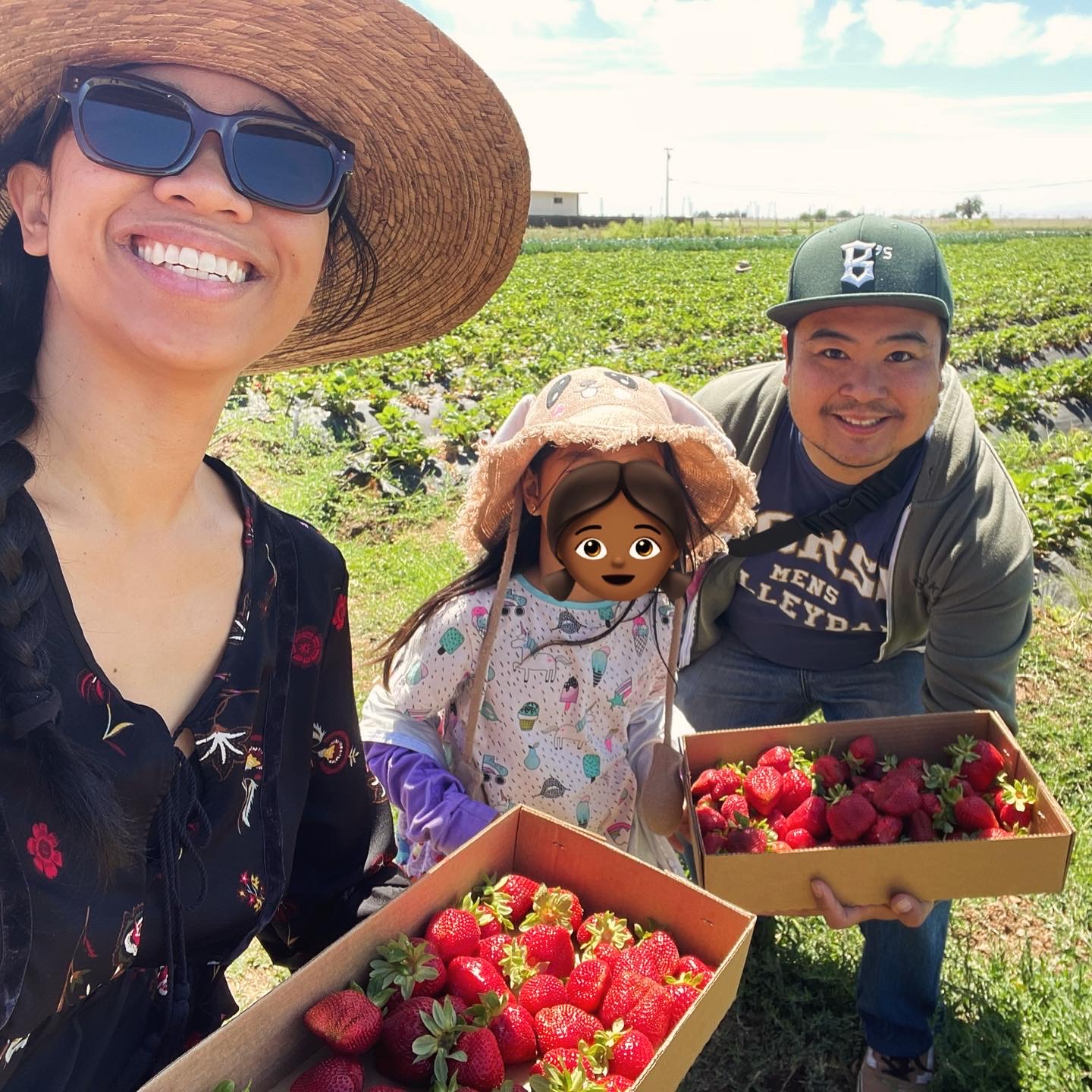 Jelly, her kid, and her partner smile at the camera while holding boxes full of strawberries