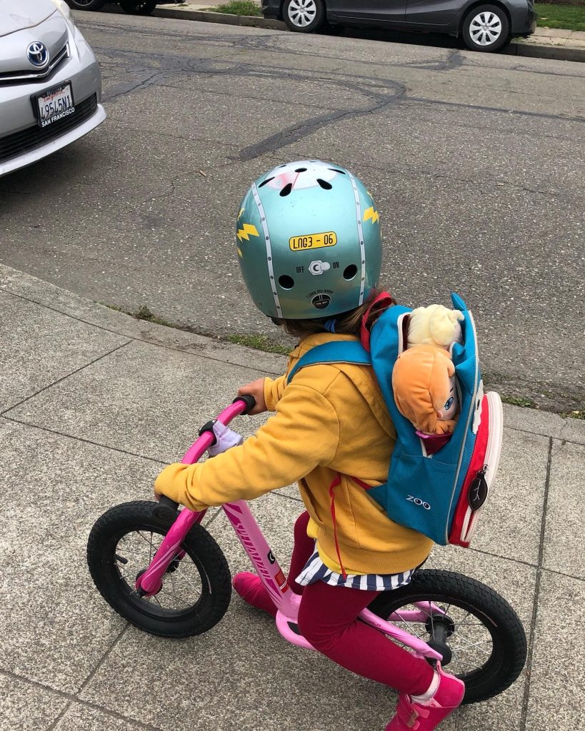 A child on a Specialized balance bike with dolls in her backpack