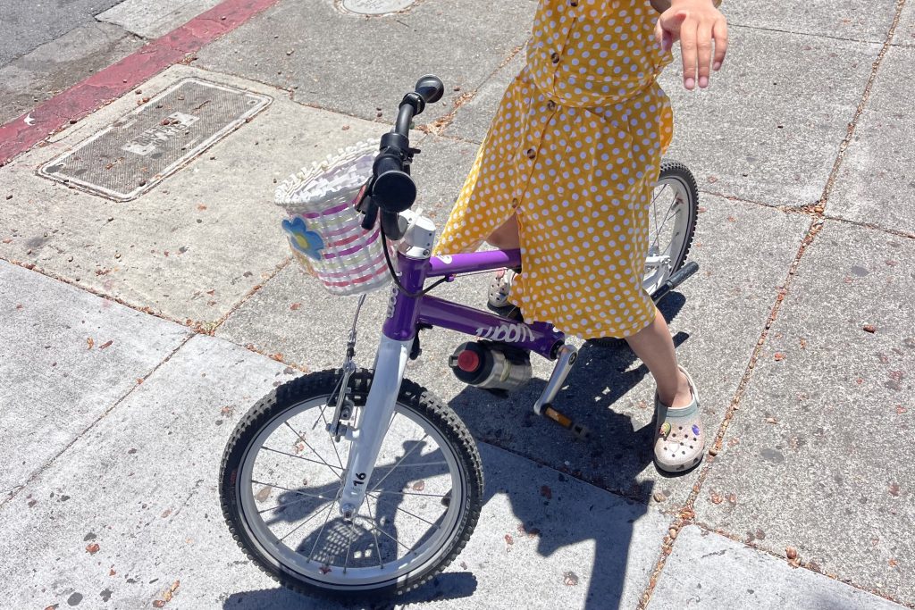 A child wearing a yellow dress sits atop a purple woom bike.