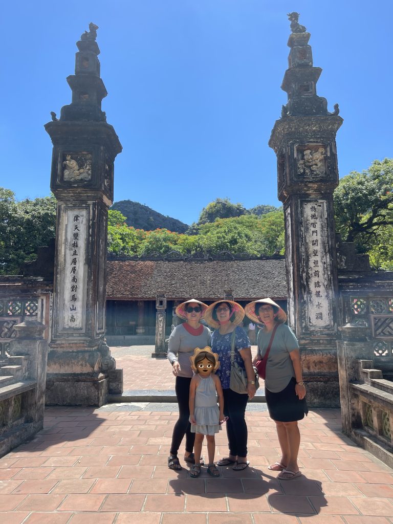 a family of three women and a young girl smile in front of the stone pillars and archways of Hoa Lu temple