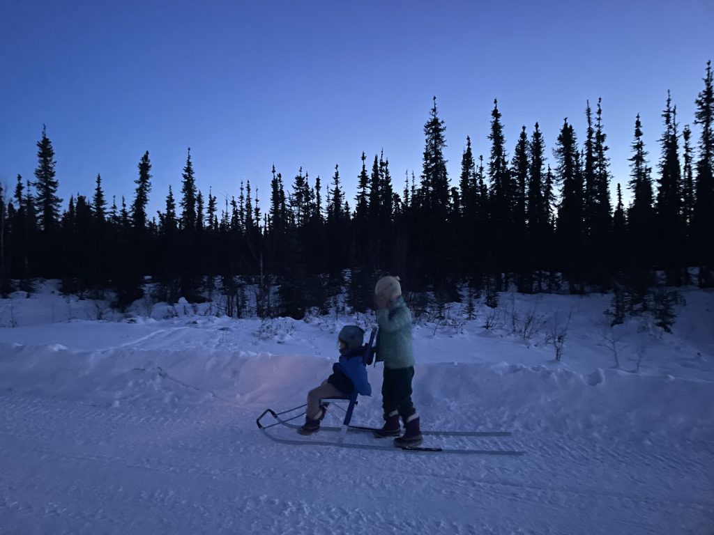 A child pushing another child on a sled during sunrise at Borealis Basecamp in Fairbanks Alaska