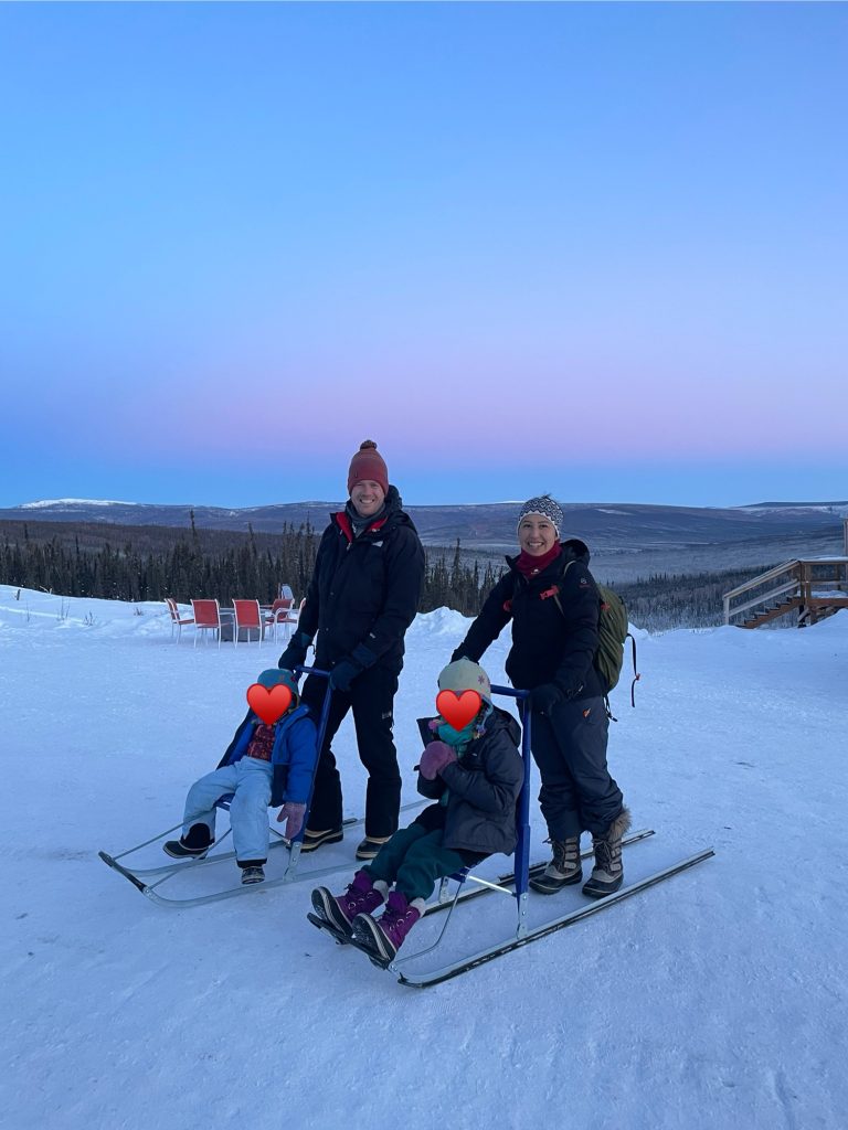 Two adults riding sleds with kids during sunrise at Borealis Basecamp in Fairbanks Alaska