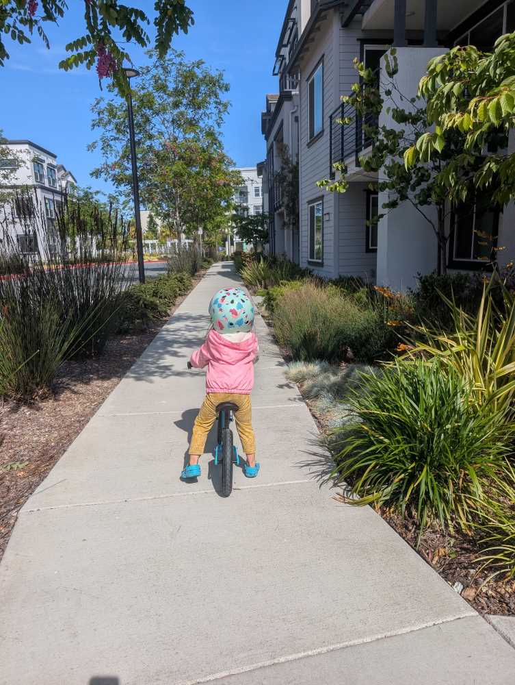 A child on a Hornit AIRO balance bike in Alameda, CA with a pink jacket