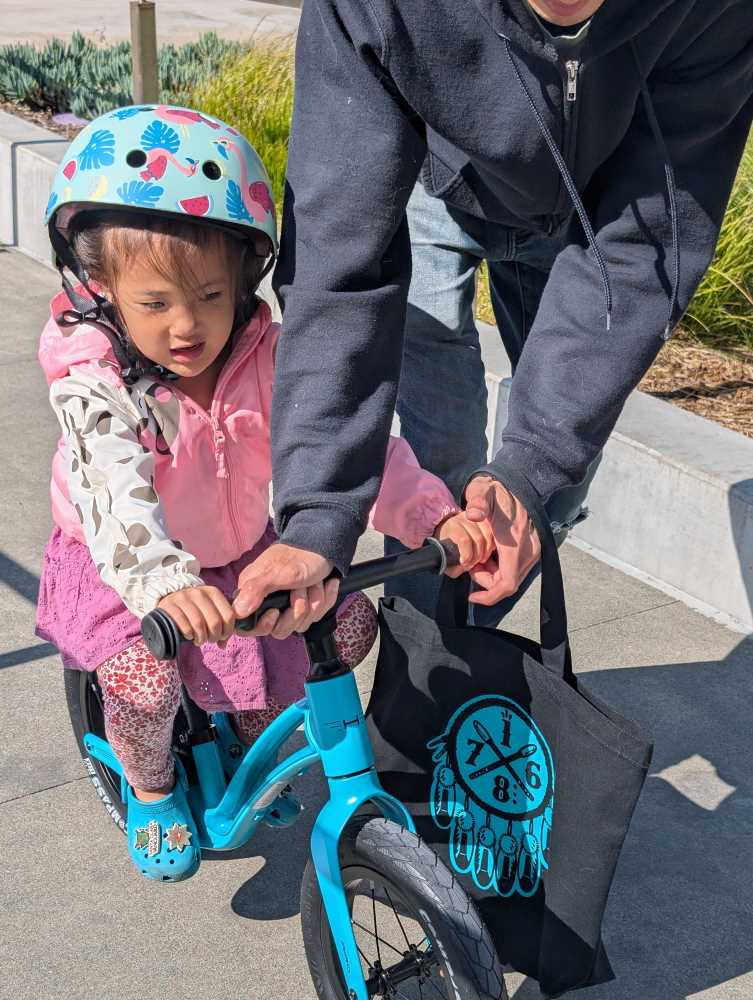A child riding a teal Hornit Airo balance bike using the footrest in matching crocs