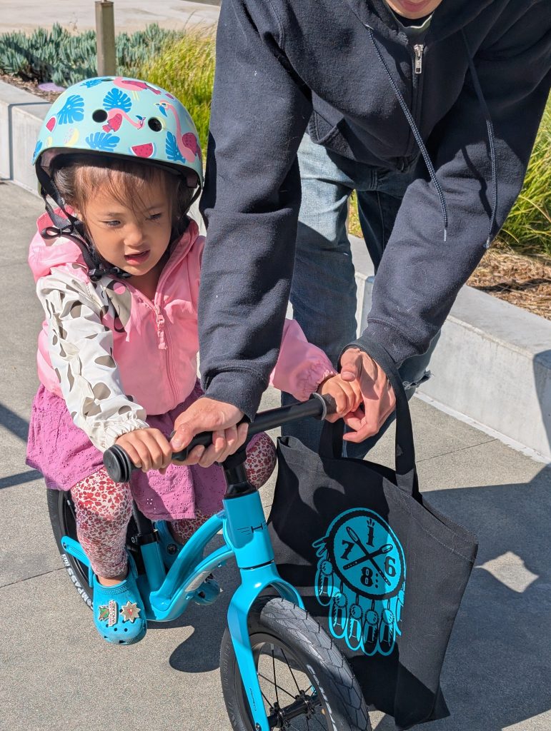 A child riding a teal Hornit Airo balance bike using the footrest in matching crocs