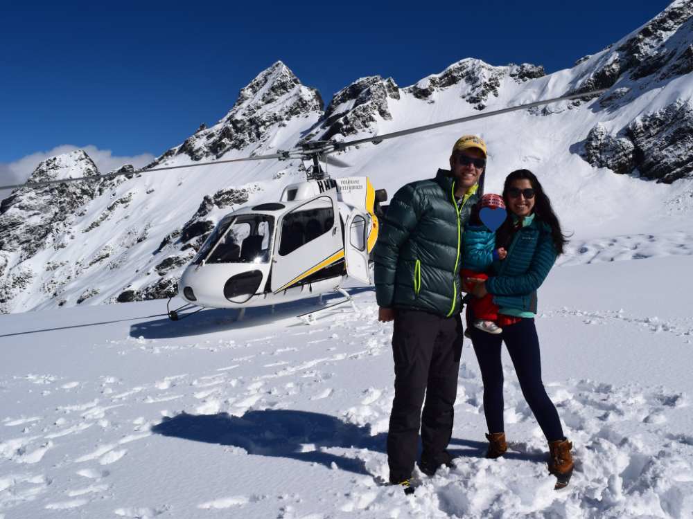 A family holding a baby in the snow in front of a helicopter in Franz Josef, New Zealand