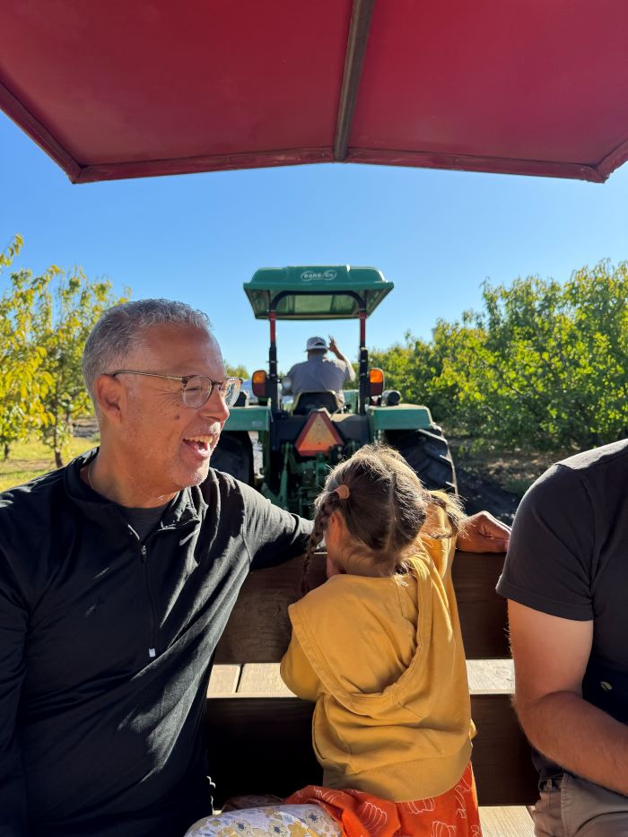 An adult laughing with a grandchild in yellow on the tractor to Three Nunns Farm in Brentwood, CA