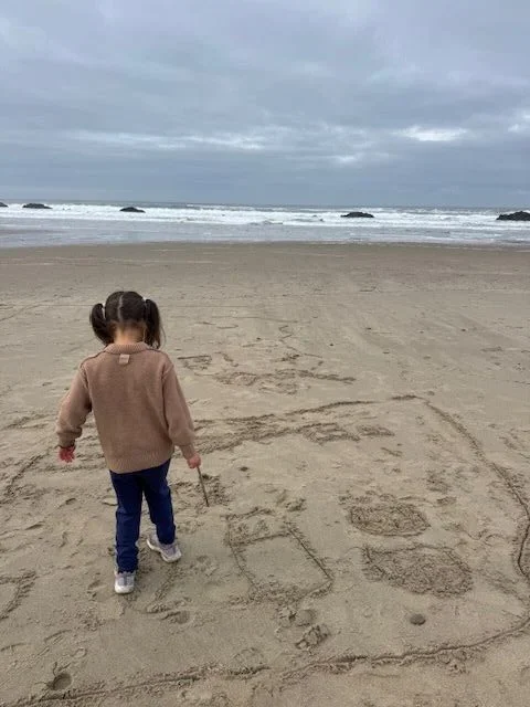 A child drawing in the sand in front of the Chinook Winds Casino Resort building in Lincoln City, OR