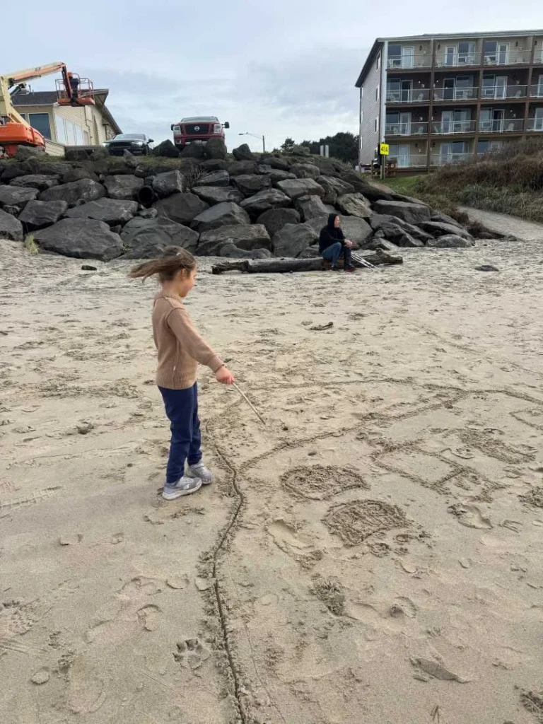 A child twirling on the beach in a taupe sweater in front of Lincoln City's Chinook Winds Casino Resort