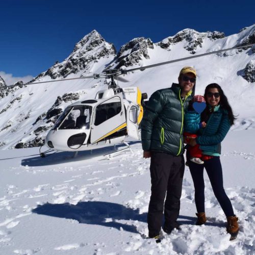 A family holding a baby in the snow in front of a helicopter in Franz Josef, New Zealand